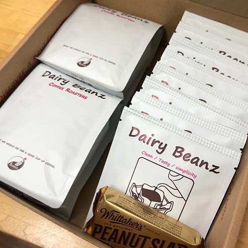 Two bags of coffee beans and coffee drip bags with a chocolate bar in a stylish gift box, part of the Custom Coffee Gift Pack with personalized labels.